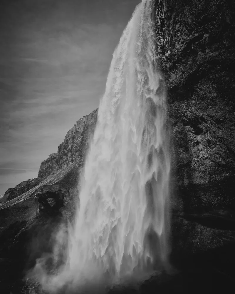 Seljalandsfoss — a monochrome photograph of the waterfall falling past a dark rock face. Plate I, Series One.
